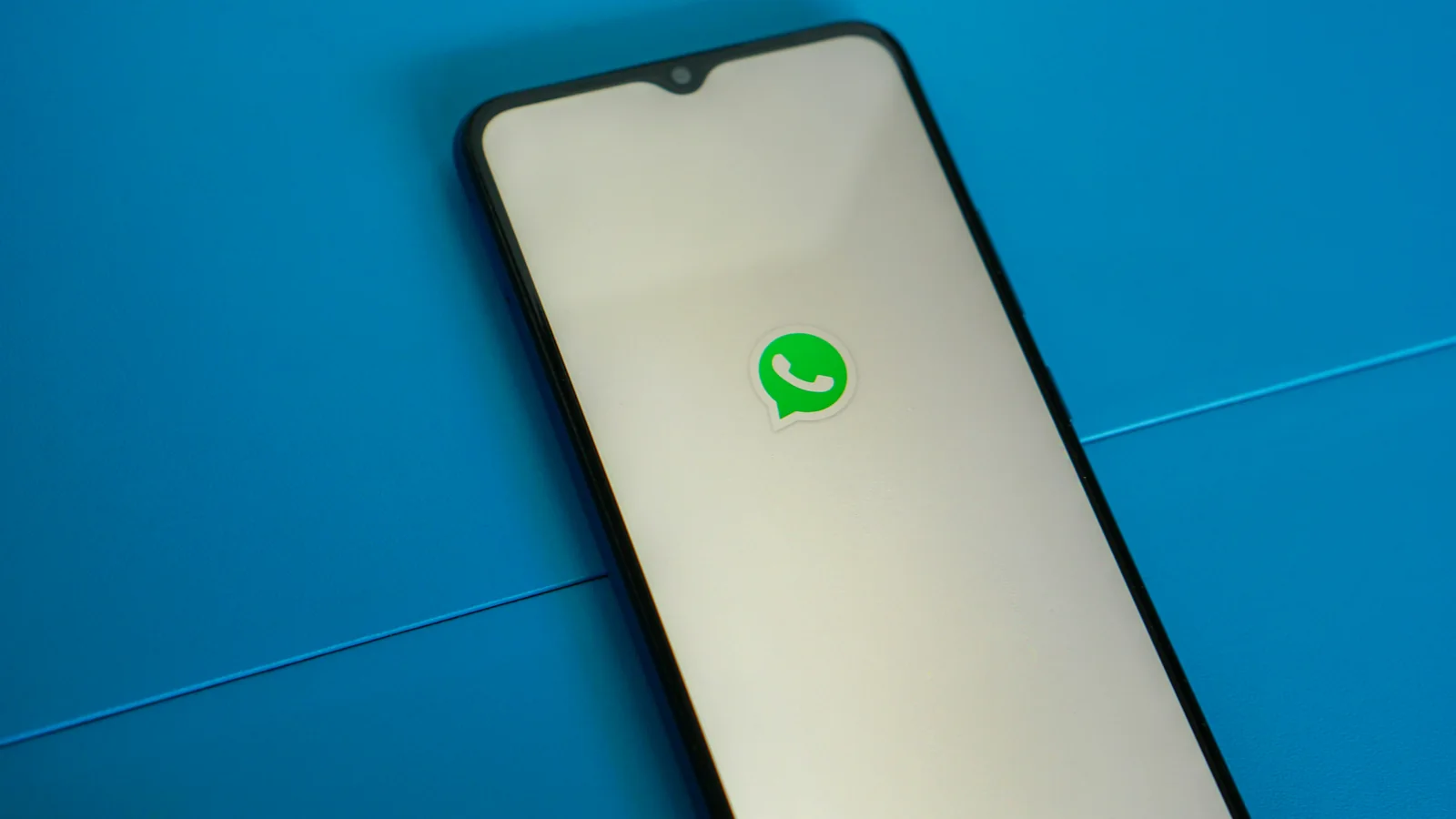 Smartphone exibindo o símbolo do WhatsApp sobre fundo azul