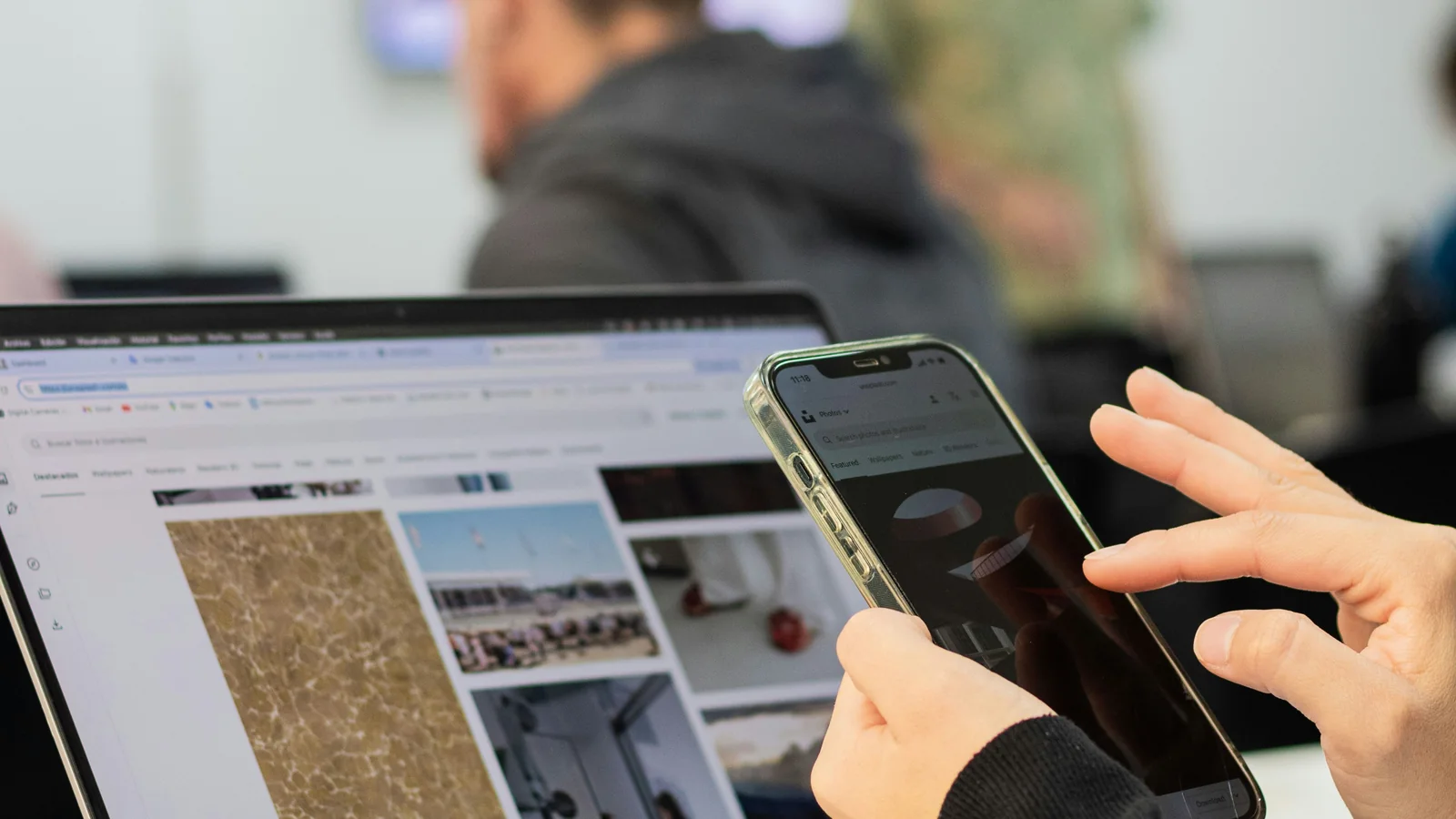 Pessoa usando smartphone ao lado de notebook durante navegação em um site